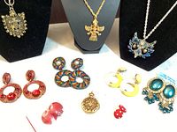 Photo showing most of the jewelry laid out including red circular earrings, multicolor beaded earrings, yellow and white earrings, teal chandelier earrings, poison ring, red dome earrings, and ladybug pins