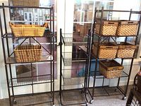 Two black metal shelving units with wire shelves on caster wheels next to rolling black metal basket shelf with four wire baskets, numerous wicker baskets placed for storage.