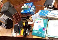 Photo of office supplies showing Fellowes shredder, Bell Howell USB lamps, organizers, label packs, tape rolls, envelopes, file folders, and miscellaneous items on desk