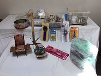 View of sewing tools and accessories arranged on table including pin cushions shaped as chairs, tub containers of buttons, ruler, scissors, and the green carrying case for sewing machine.