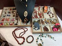 Display of several jewelry items on trays and necklace bust including bead and pendant necklaces, bracelets, and assortments of earrings.