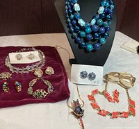 Full display of assorted vintage costume jewelry laid on white and burgundy velvet surfaces, including necklaces on bust and various earrings, bracelets, and brooches laid flat.