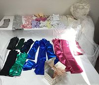 Wide view of all gloves laid out showing variety of materials and colors including satin, lace, leather, and a wedding hat with tulle and hair combs.