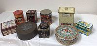 Overview of 10 assorted vintage tins of various shapes, sizes, and colorful decorative prints on a white background.