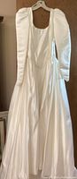 Full view of one white vintage wedding dress hanging showing puffed long sleeves and full skirt