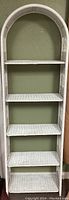 Front view of white wicker shelving unit showing five shelves and arched top.