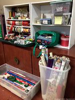 Photo of two white shelving units holding numerous spools of ribbons in various colors and widths, bows, and gift bags. Rolls of wrapping paper stored in plastic bins below the shelves.