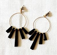 Pair of 10K yellow gold hoop earrings with five black onyx tapered bar dangles each, laid flat on white fabric background. Shows the front view clearly.