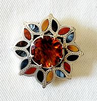Front view of antique sterling silver brooch showing large faceted citrine center stone and colorful natural stone inlays in a floral design