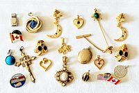 Photo showing assortment of charms, pendants, and pins on white background including Canadian flags, crescent moons, crosses, hearts, and decorative charms.