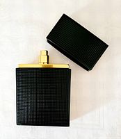 Black textured 100 ml perfume bottle with a gold spray nozzle, cap removed and placed beside it on a white background.