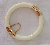 Top view of hinged bangle bracelet showing white circular body and gold metal hinge with safety chain.