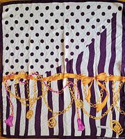 Full view of the scarf laid flat, showing the pattern with purple polka dots and stripes, gold chains and ribbons crossing horizontally.