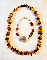 Photo of natural amber nugget bead necklace and sterling silver bracelet with engraved medallion laid flat on white surface.