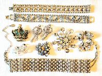 Full view of all nine rhinestone jewelry pieces laid out on white fabric background showing bracelets, brooches, earrings, and a crown-shaped pin.