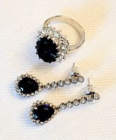 Ring and earrings set laid flat on fabric showing dark blue stones and diamond-like crystals in silver-tone metal settings.