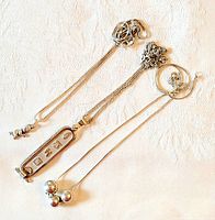 Three sterling silver necklaces laid out showing pendant designs: Egyptian motif rectangular pendant, triple silver spheres pendant, small baby-shaped pendant on delicate chain.