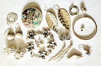 Various sterling silver jewelry items including earrings, pendant, and bracelet arranged on white fabric, showing different styles and details