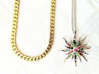 Gold-tone curb chain next to silver-tone starburst pendant necklace lying on fabric