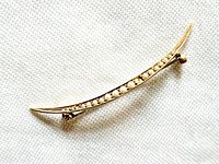Front angled view of curved brooch showing gold frame and seed pearls