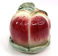 Front view of vintage sliced apple pottery jam jar showing red and green glazing and leaf top with painted details.