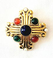 Front view of vintage Maltese cross brooch showing gold tone metal with multicolored lucite cabochons and white pearl-like accents on a fabric background.