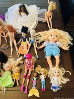 Mixed lot of Barbie and other dolls arranged on table with varying sizes and outfits including wedding dress, swimsuits, and casual wear.