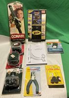 Photo showing all items from seller's lot including Conair Instant Heat Styling Iron box, Tool Band-It box, OfficeMax pliers, rubber floor savers, tabletop easel manual, paper punch, drink holder, and Griffin case.