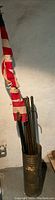 Full view of vintage red and white striped flag on wooden pole leaning against wall with wooden walking canes and metal stand