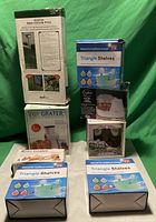 Photo of 8 boxed items against green backdrop, including Step-In Bird Feeder Pole, 3 Triangle Shelves, 3 Easy Graters, and 1 white food chopper