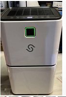 Front view of white dehumidifier showing digital display with green light and touch controls on top black panel.