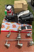 Lot displayed on blanket outdoors showing black stage spotlight fixtures with barn doors, a ceiling light fixture with six silver spotlights, and boxed emergency sign and towing mirror.