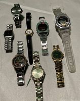Full view of 8 assorted men's and women's watches laid out side by side showing variety in band materials, face shapes, and styles.