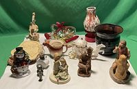 Full view of the mixed lot showing various figurines, glass and ceramic decorative items on a white surface with green background.