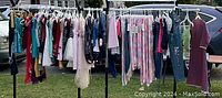 Full view of kids clothes hanging on racks outdoors, showing the variety of clothes and colors available in this lot.