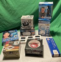 Photo of all items in original packaging arranged on green background including digital photo frame, photo coaster set, VR viewer box, bladeless fan speaker box, calendar towel, hanging chalkboard, AM/FM radio button and Vivitar headphones.