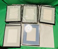 Photo showing a collection of nine picture frames, eight predominantly black matted frames and one brown framed with blue mat, all size 8x10, new in plastic wrapping.