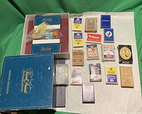 Top view of Trivial Pursuit Master Game Genus Edition box with contents visible including game cards, dice, and playing pieces, alongside 13 assorted vintage playing card packs arranged on a white surface.