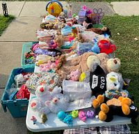 Overview of vintage Barbie dolls, stuffed animals and assorted toys on a table outdoors
