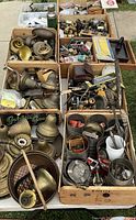 Overview of wooden crates filled with various vintage brass hardware including lamp sockets, door knobs, light fixture parts, and small metal fittings organized loosely in multiple boxes.
