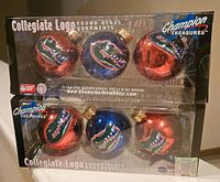 Two unopened sets of Champion Treasures Florida Gators collegiate logo round glass ornaments, each set contains three glass ornaments in blue and orange colors.