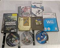 Multiple untested video game discs and cartridges including Tom Clancy's Ghost Recon for GameCube, NBA March Madness 2003 for PlayStation, Disney Epic Mickey for Wii, and The Legend of Zelda NES cartridge among others.