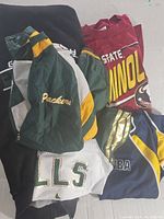 Assorted sports clothing including Packers jacket, Seminoles shirt, Bulls and NBA jerseys.