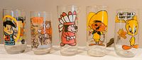 Five vintage glasses featuring Freddy Flintstone, Star Wars characters, cartoon Indian, Speedy Gonzales, and Tweety Bird, showing condition and designs.
