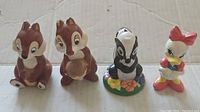 Four vintage Disney ceramic figurines on cardboard background; including Chip, Dale, Flower, and Daisy Duck