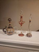 Three vintage Egyptian perfume bottles with decorative gold and colored glass patterns, measuring about 6 inches tall, arranged on a surface.
