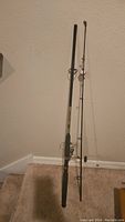 Full view of the fishing rod and reel standing upright, showing rod length, foam handle, and attached reel.