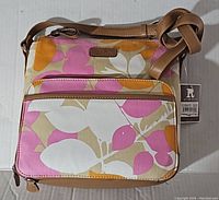 Front view of square-shaped purse with floral pattern and front zipper pocket with leather trim, adjustable leather strap, and attached brand tag.