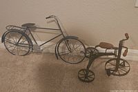 Photo showing both metal bicycle sculptures against a wall on carpeted floor.