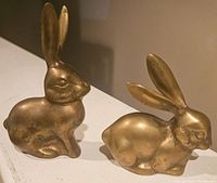 Side view of one brass rabbit figurine showing detailed face and upright ears.